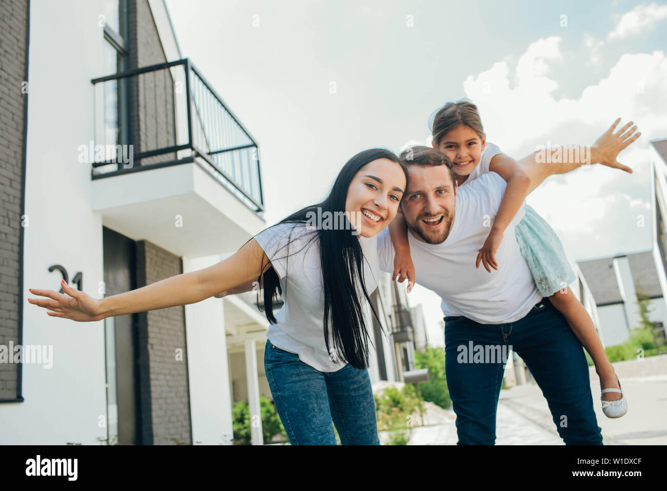 Famiglia giocando con la figlia, bambino piggyback ride su padre torna, hanno alzato le mani come volare Foto Stock