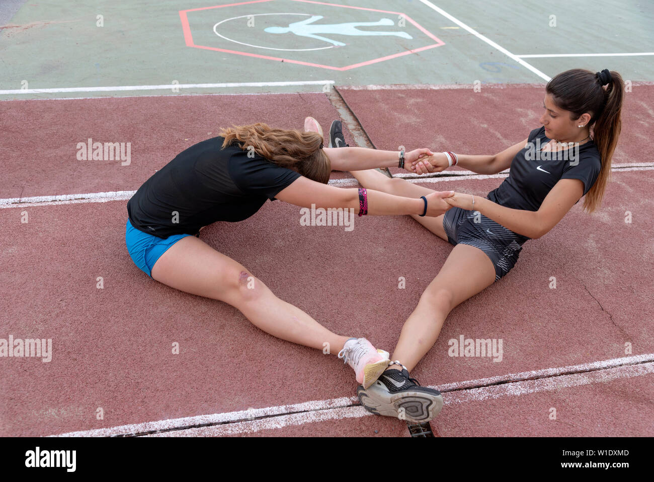 Creta, Grecia. Giugno 2019. Due giovani atleti seduti sulla lavorazione del terreno con gambe e costretto spilts movimento, Foto Stock