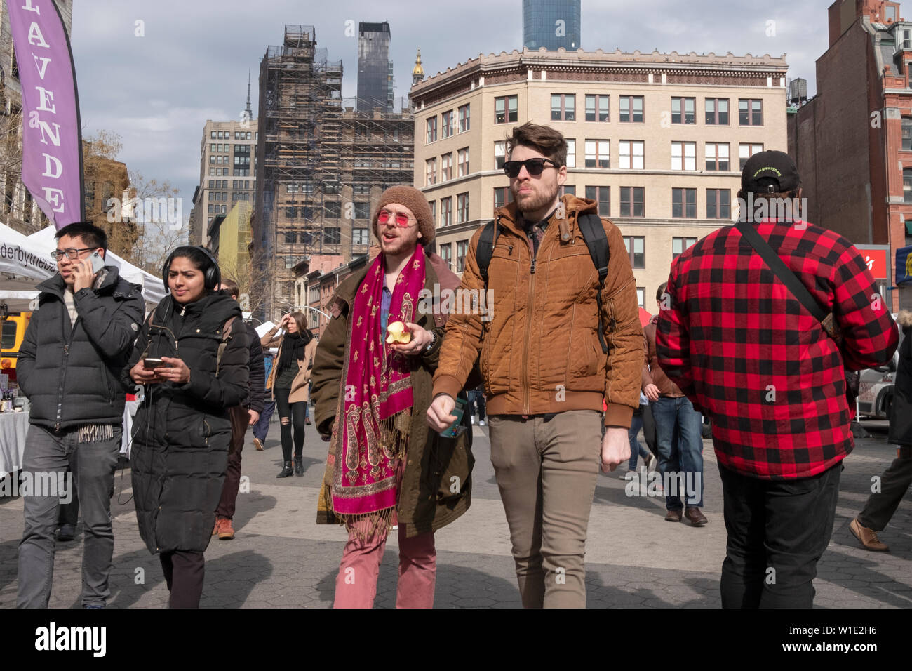 Un uomo di mangiare un Apple passeggiate attraverso la Piazza Unione Mercato verde con un amico. La città di New York, l'inverno 2019. Foto Stock