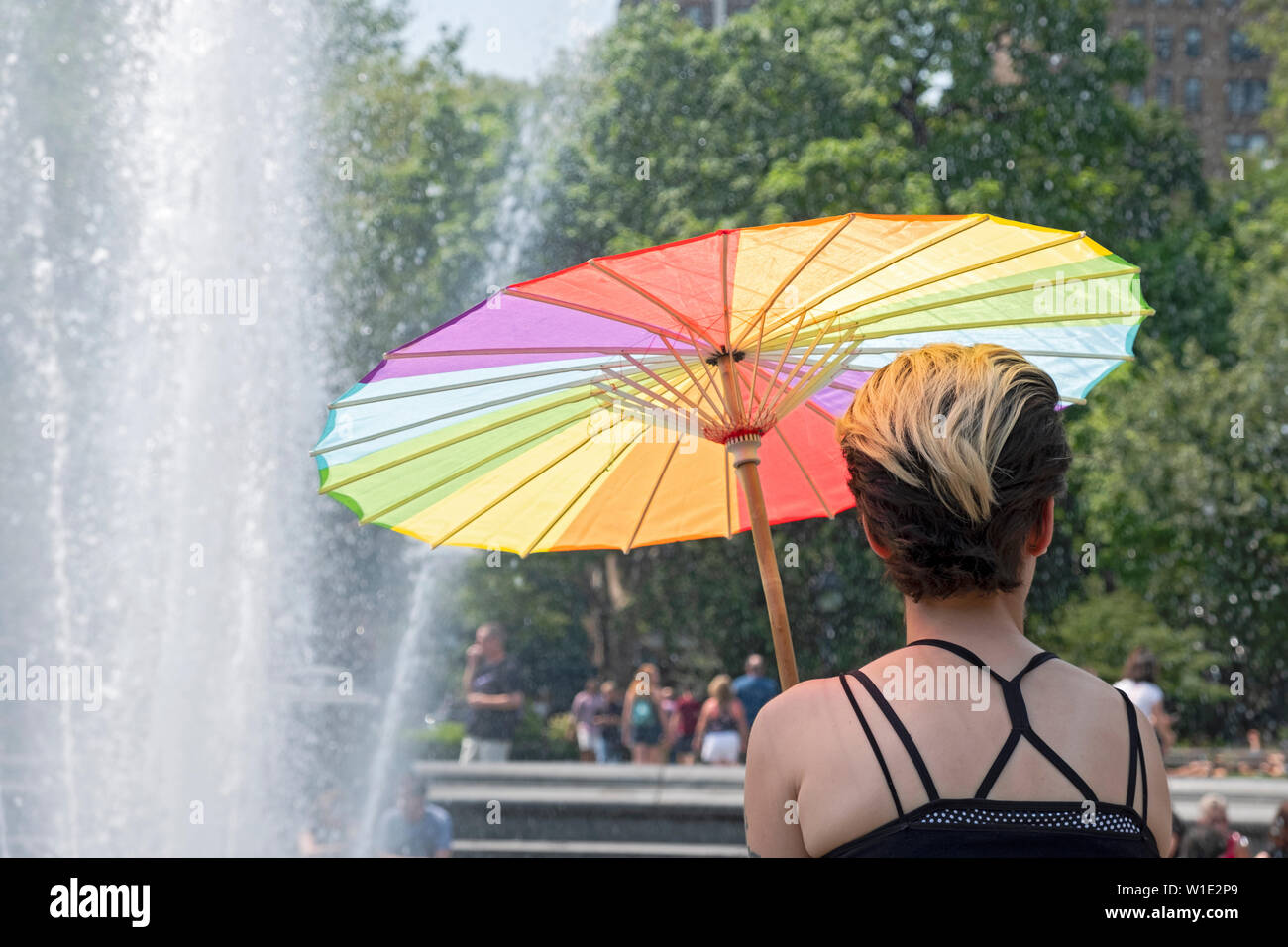 Una donna si siede presso la fontana di Washington Square Park con un ombrello che ha il LGBT arcobaleno di colori. Il giorno della Trans giorno di azione Rally. Foto Stock