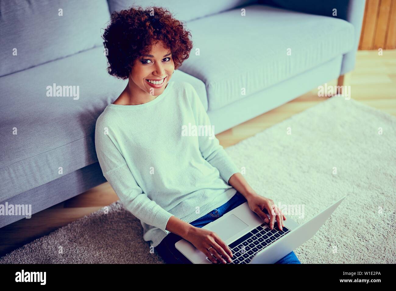 Felice giovane donna africana con laptop seduto in soggiorno - foto con colori filtrati Foto Stock