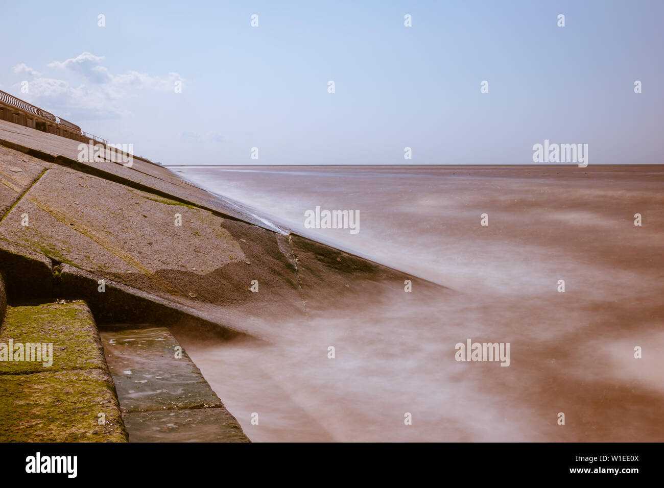 Una lunga esposizione dell'acqua di mare e le onde di colpire una pendenza revetment in calcestruzzo o seawall come parte del litorale le misure di difesa contro le inondazioni Foto Stock