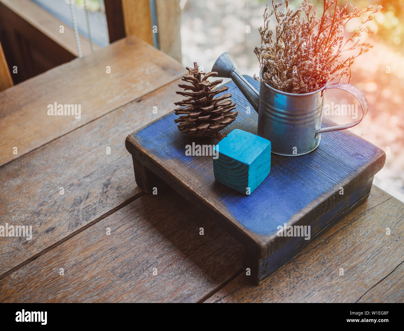 Gli oggetti di legno, blu cubica, pigne e fiori secchi in piccoli annaffiatoio decorazione su un tavolo di legno. Foto Stock
