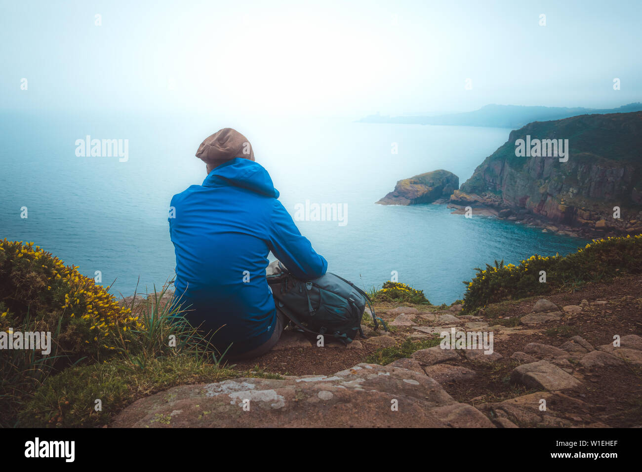 Escursionista giovane uomo seduto con il suo zaino sul bordo di una scogliera a contemplare la paesaggistica costa paesaggio. Viaggiare, Stile di vita, concetto all'aperto Foto Stock