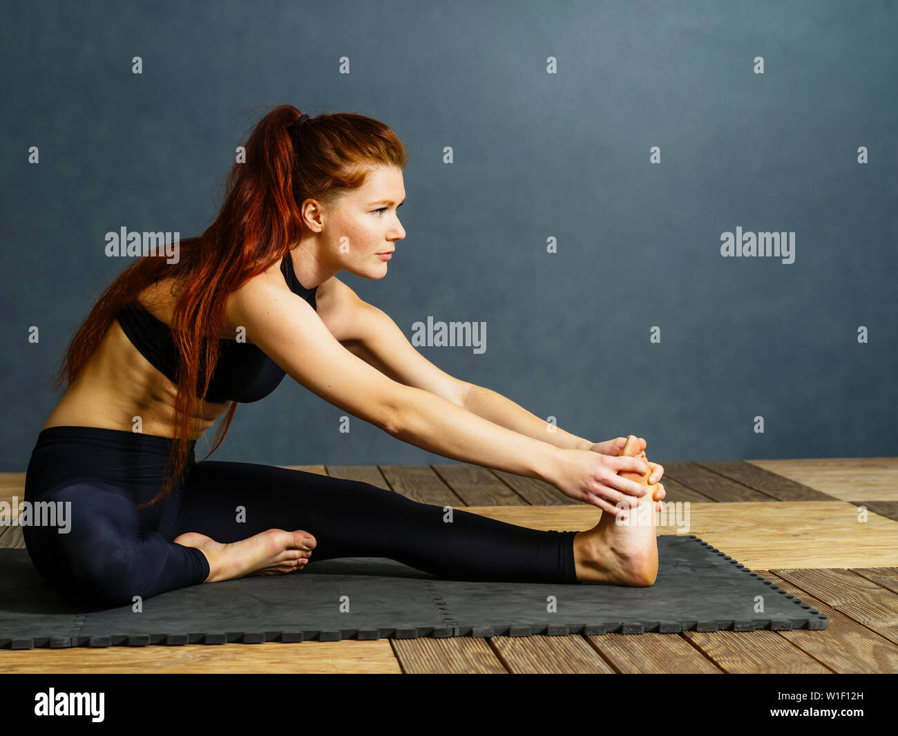 Foto di una bella redhead stretching femmina sul pavimento seduta su un tappetino. Foto Stock
