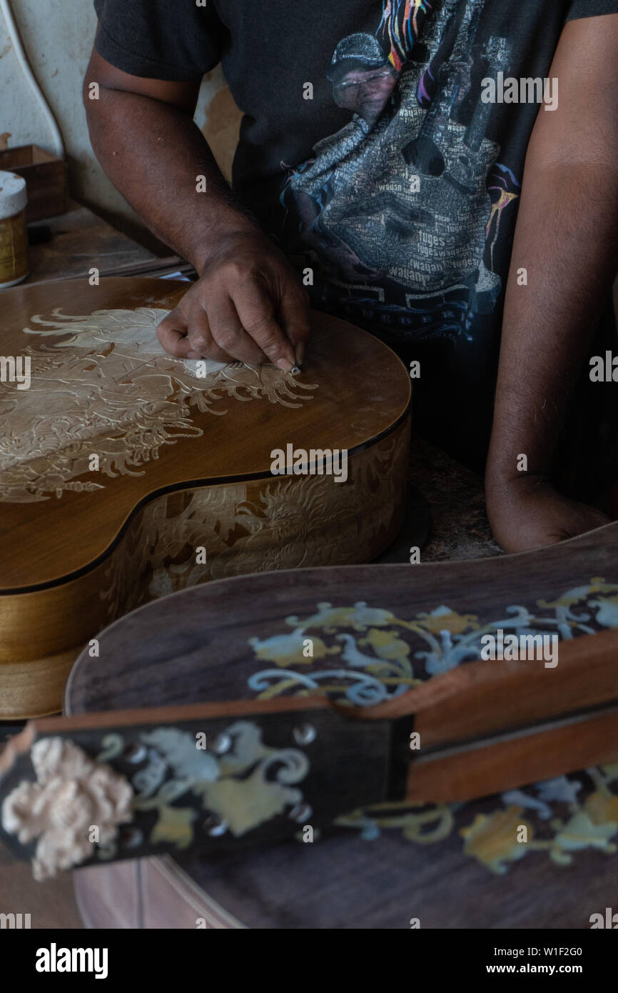 Una chitarra artigiano sono carving a chitarre classiche in legno, con pattern balinese, in una chitarra in legno workshop presso Guwang Village, Gianyar Bali Foto Stock