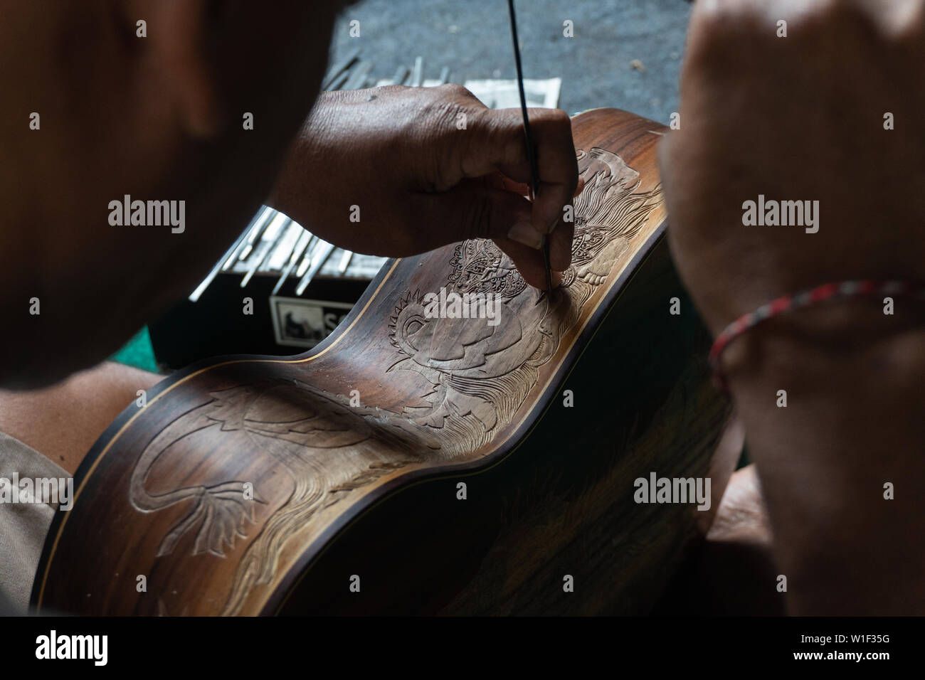 Una chitarra artigiano sono carving a chitarre classiche in legno, con pattern balinese, in una chitarra in legno workshop presso Guwang Village, Gianyar Bali Foto Stock