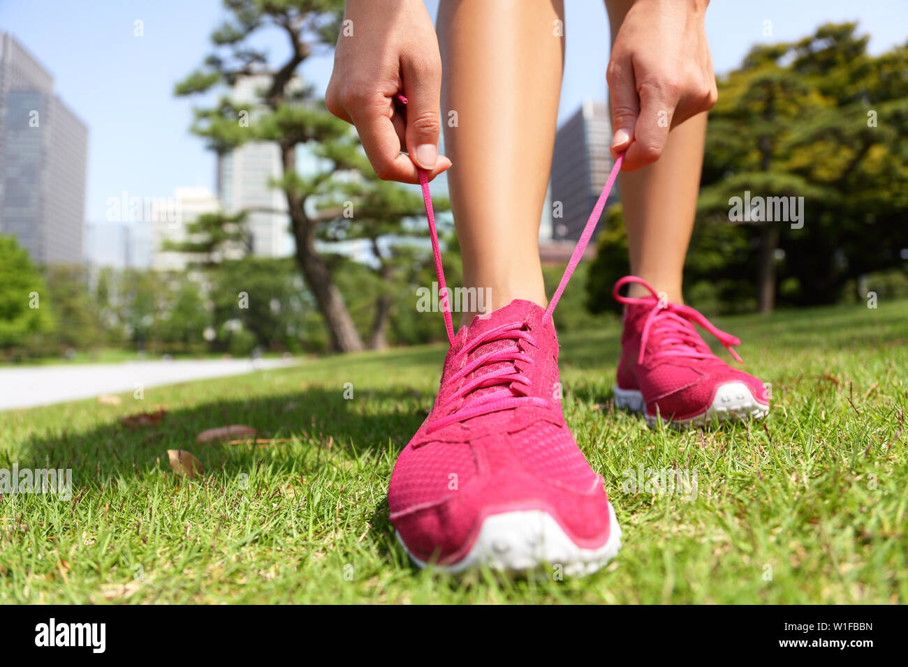 Runner pronti per fare jogging legatura di scarpe running Laces - Donna preparazione prima di eseguire la messa su formatori in giapponese parco vicino a Ginza a Tokyo, Giappone Foto Stock