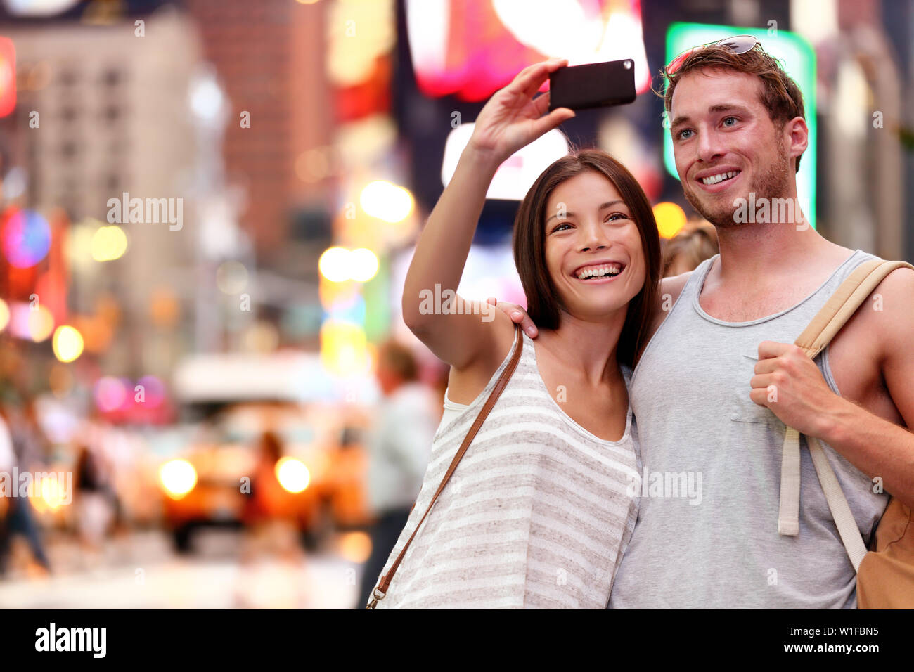 Travel Tourist giovane tenendo selfie con lo smartphone in New York City, Stati Uniti d'America. Self-portrait foto su Times Square di notte. Bella giovani turisti divertendosi, Manhattan STATI UNITI D'AMERICA. Donna asiatica, uomo caucasico Foto Stock