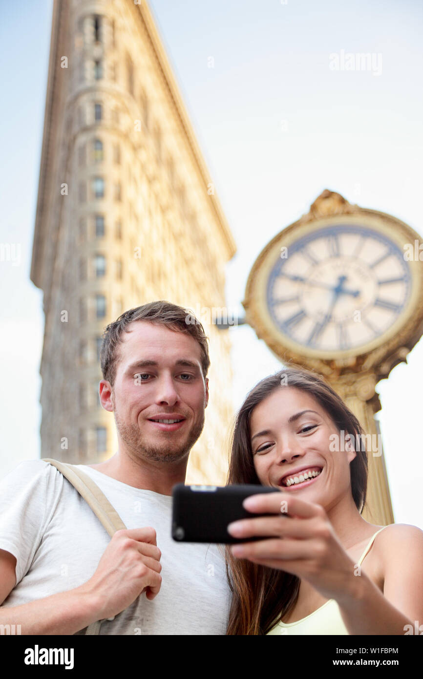 Coppia di viaggio prendendo selfie nella città di New York New York, Stati Uniti d'America. I turisti holding smartphone per fotografia autoritratto nella parte anteriore del famoso Flatiron Building downtown in estate. Foto Stock
