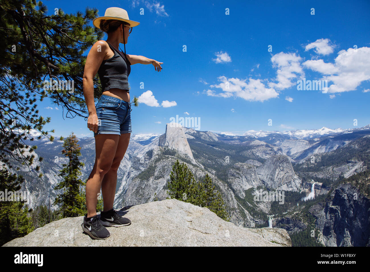 Donna caucasica turistica nei suoi trenta che indica le cascate del Nevada e Half Dome da Glacier Point nel Parco Nazionale di Yosemite, California, Stati Uniti Foto Stock