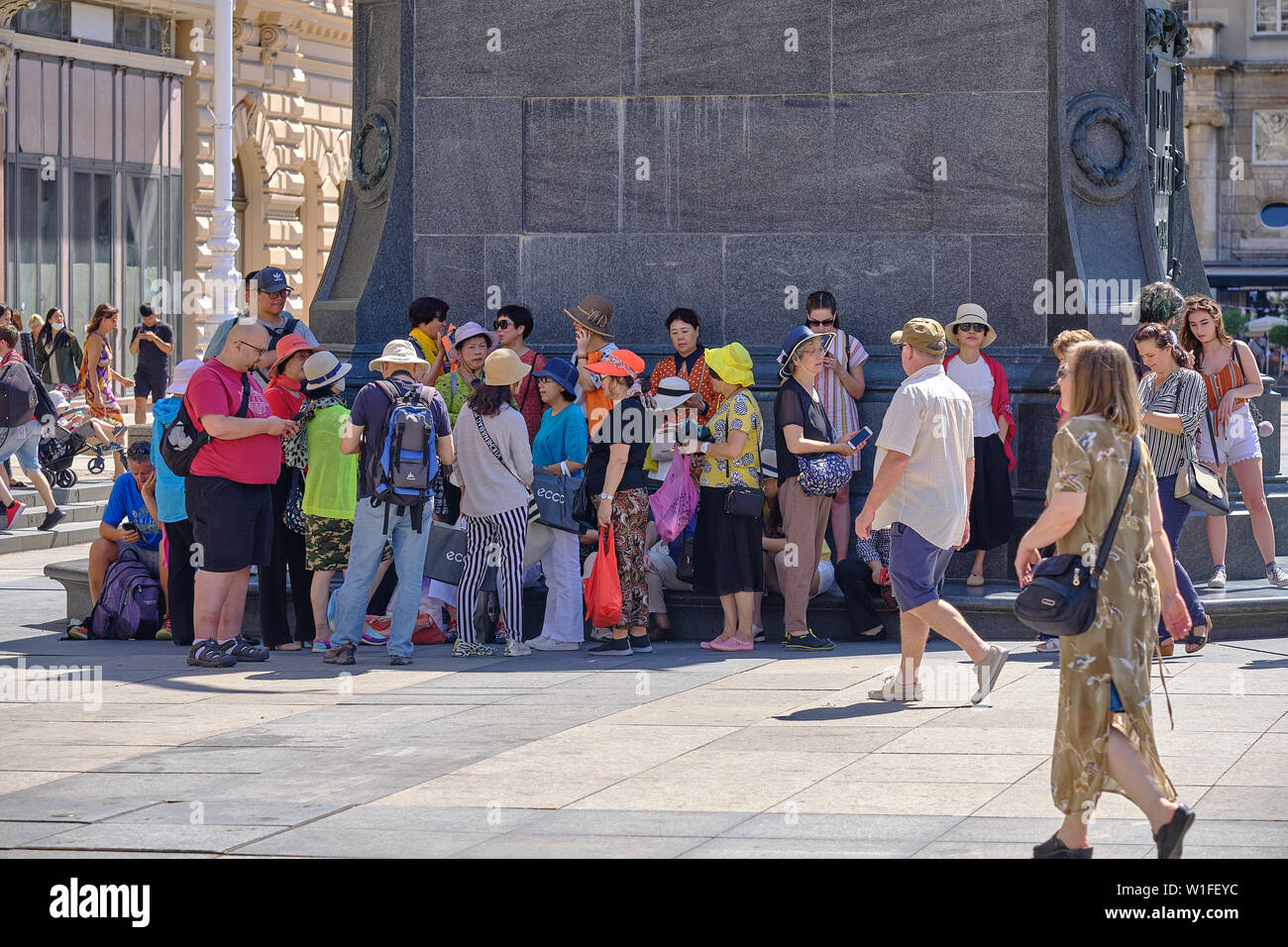 Gruppo di turisti asiatici nascondendo in piccoli spot di ombra da una statua come la temperatura raggiunge la metà degli anni trenta a Zagabria in Croazia Foto Stock