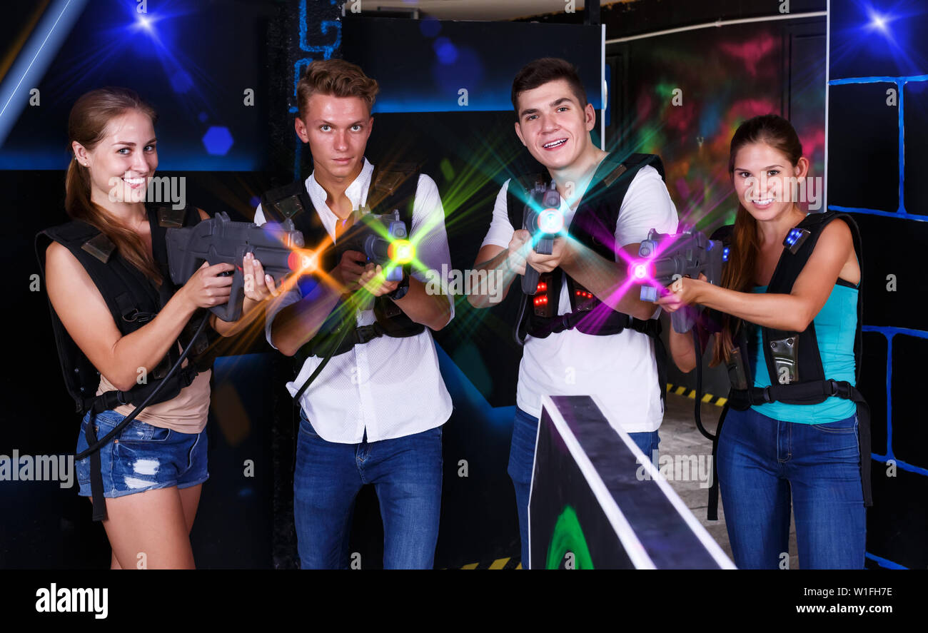Quattro felice giovane maschio femmina una posa con pistole laser nelle loro mani in scuro tag laser camera Foto Stock