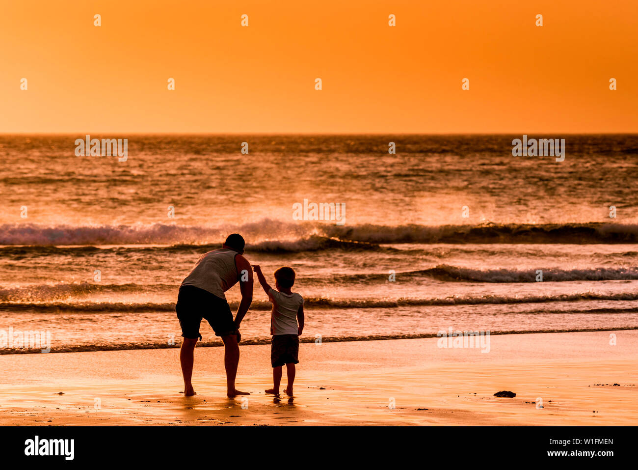 Un padre e il suo giovane figlio godendo il bellissimo tramonto su Fistral Beach in Newquay in Cornovaglia. Foto Stock