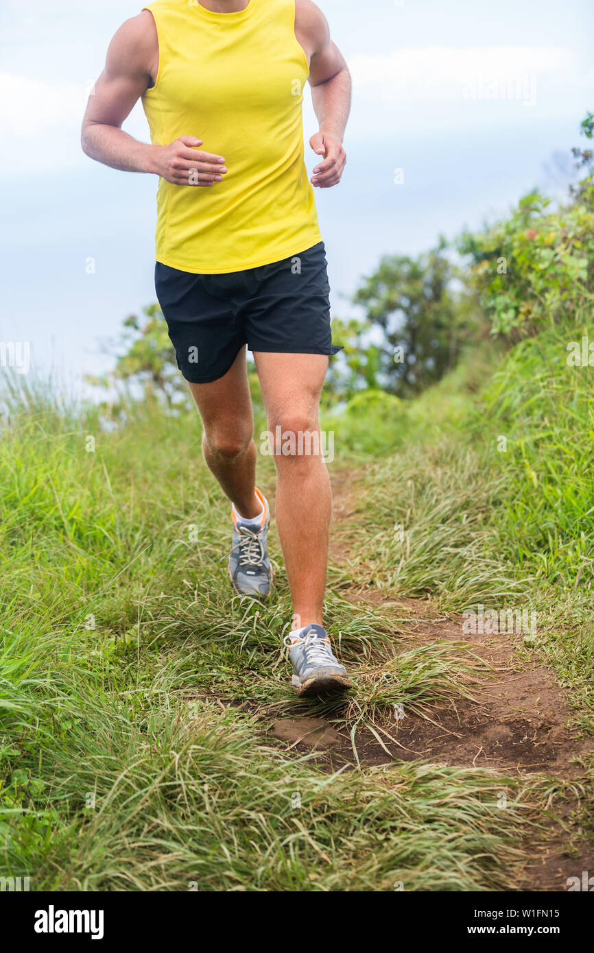 Maschio Fitness runner jogging in scarpe da corsa all'aperto in erba verde sentiero percorso. Atleta uomo allenamento cardio in natura. La parte inferiore del corpo raccolto per piedi, gambe, ginocchia il problema della salute il dolore, il concetto di abbigliamento sportswear. Foto Stock