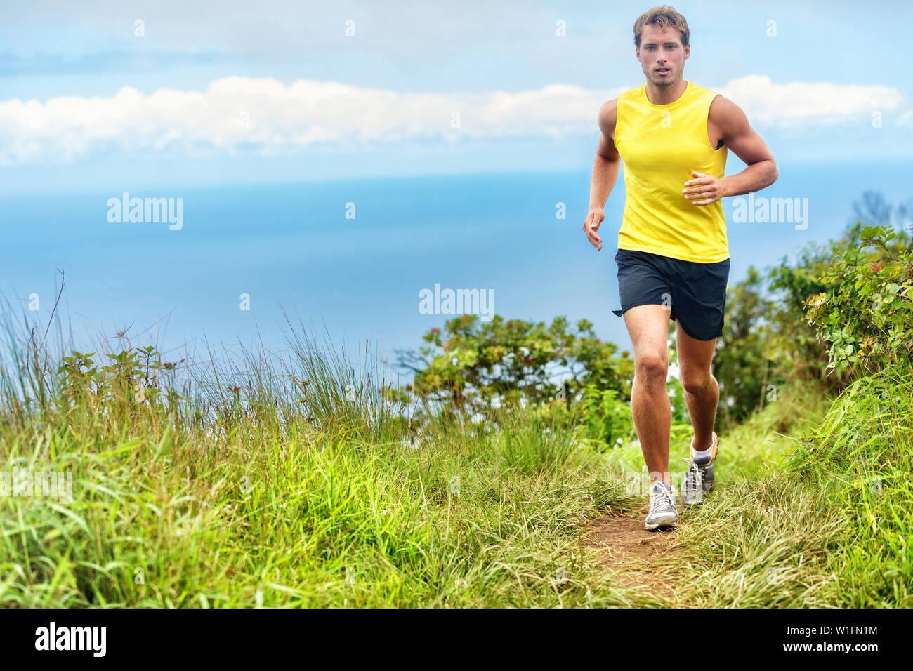 Uomo che corre runner a vivere una vita sana in uno stile di vita attivo. Voce maschile giovane atleta allenamento cardio che lavora fuori le gambe su di un sentiero percorso nel parco naturale della foresta ed erba verde in montagna con sfondo oceano. Foto Stock