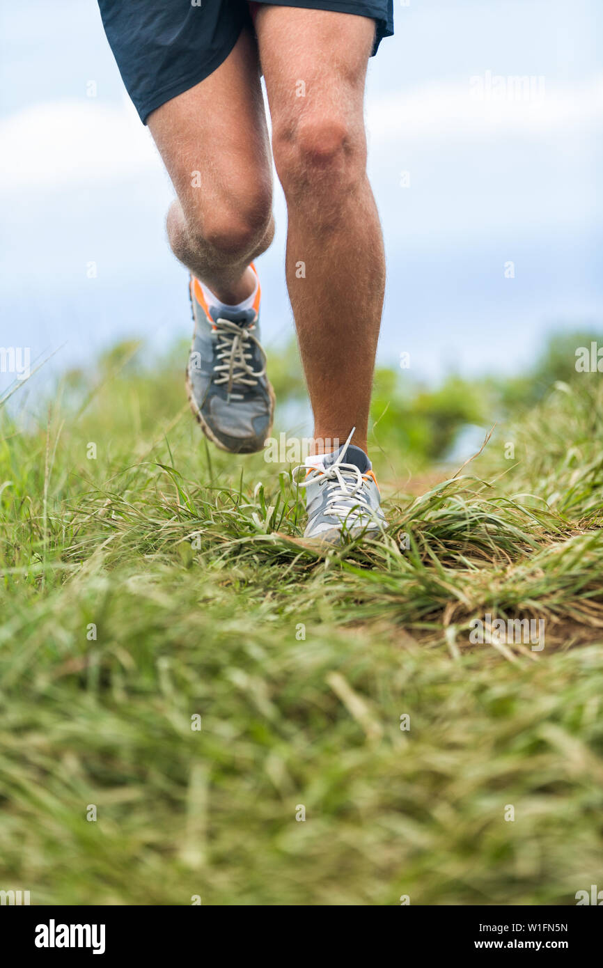 Scarpe da corsa e le gambe di runner jogging all'aperto in erba verde sentiero percorso. Montare atleta uomo che lavora fuori cardio in natura. La parte inferiore del corpo raccolto per i piedi, le cosce e le ginocchia di salute e problemi di dolore del concetto. Foto Stock