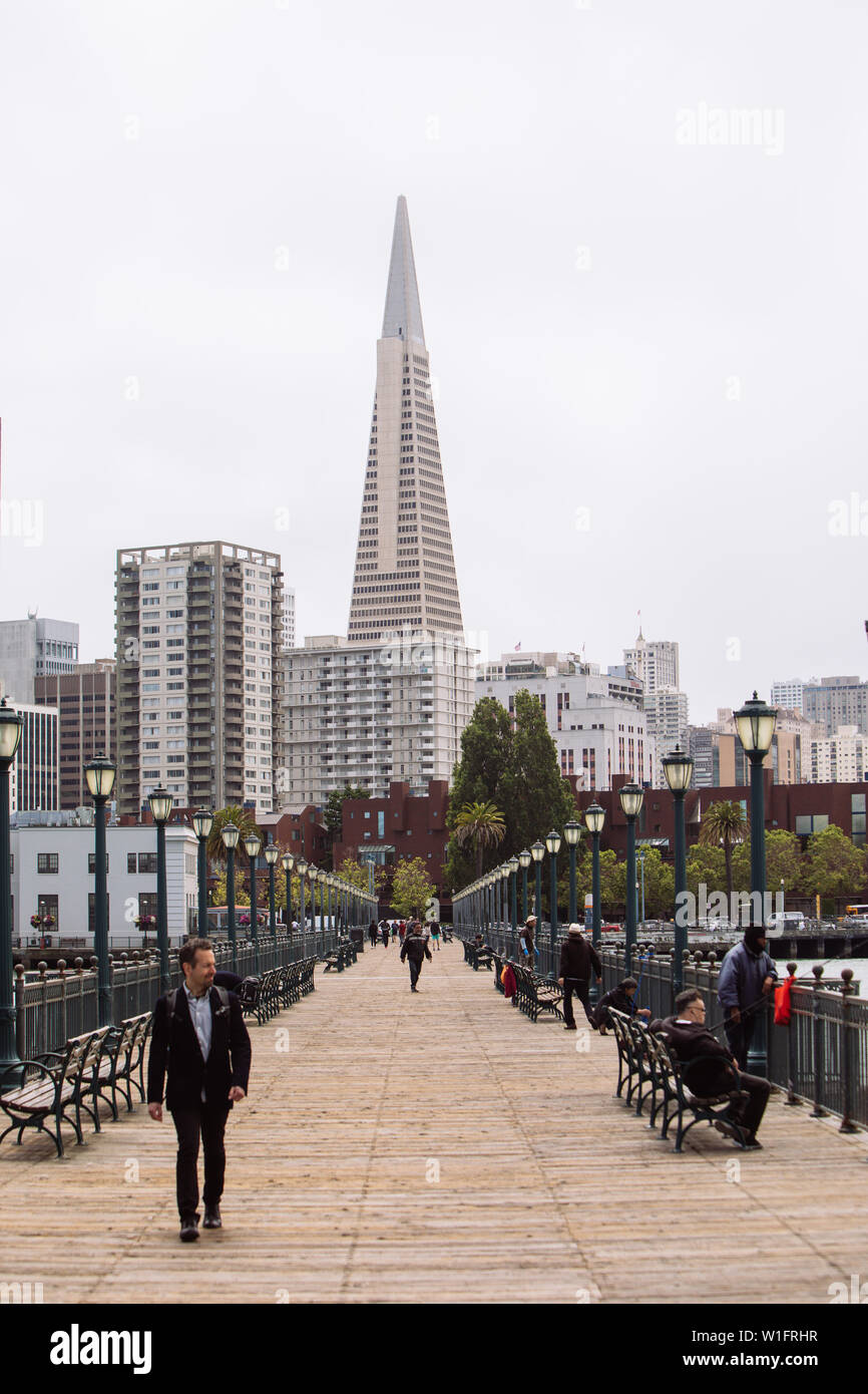 Persone che camminano sul Pier 41 Wooden Viewing Pier con il Pyramid Building centrato sullo sfondo, San Francisco, California, USA Foto Stock