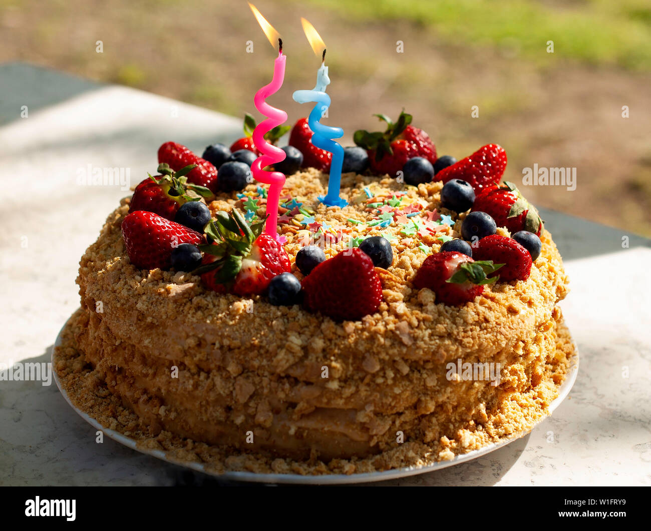 Piatti per le feste e il concetto di festa. Torte fatte in casa per il compleanno decorato con candele, mirtilli freschi, le fragole. Due anni. Foto Stock