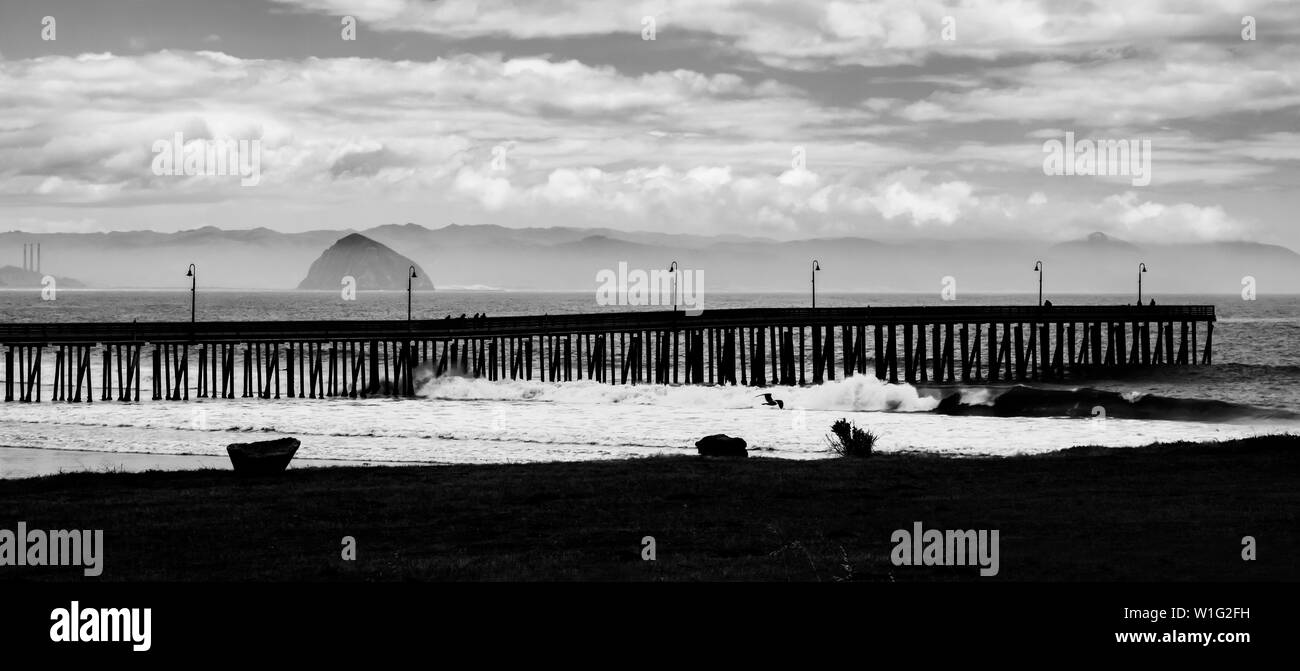 In bianco e nero del molo che si estende nel mare all Morro Rock in background in California. Foto Stock