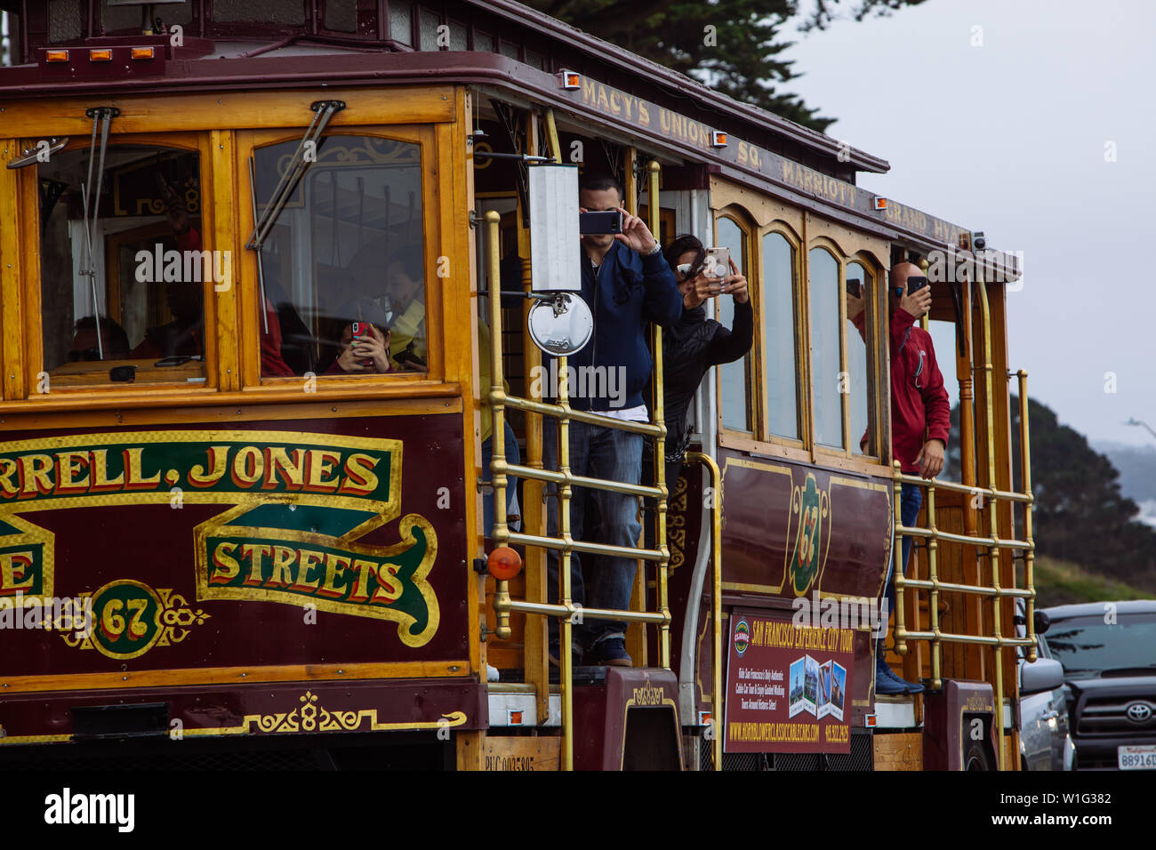 I turisti scattano foto con i cellulari durante il tour della città in tram di San Francisco, California, USA Foto Stock