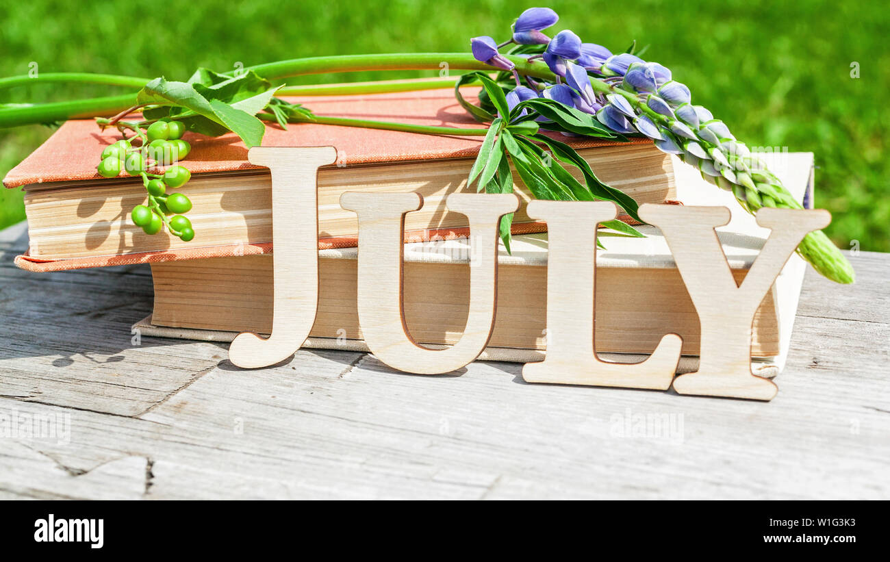 Parola luglio, una pila di libri vecchi e bouquet di fiori su un di legno bianco sfondo rustico. Composizione di estate Foto Stock