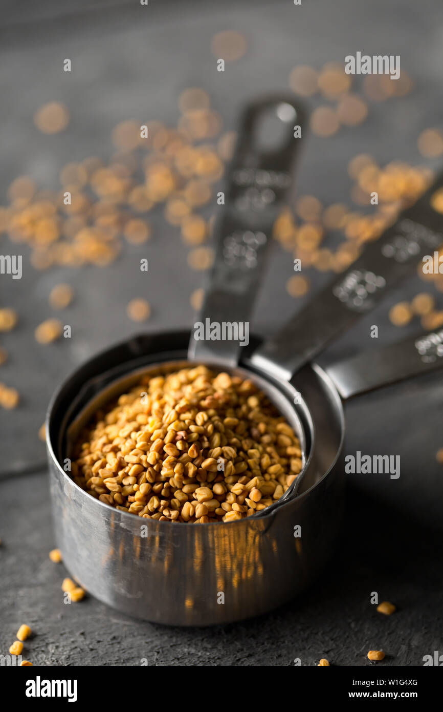 Secchi, materie fenugreek seme nel misurino on dark moody cucina nera di sfondo della tabella con il fuoco selettivo Foto Stock