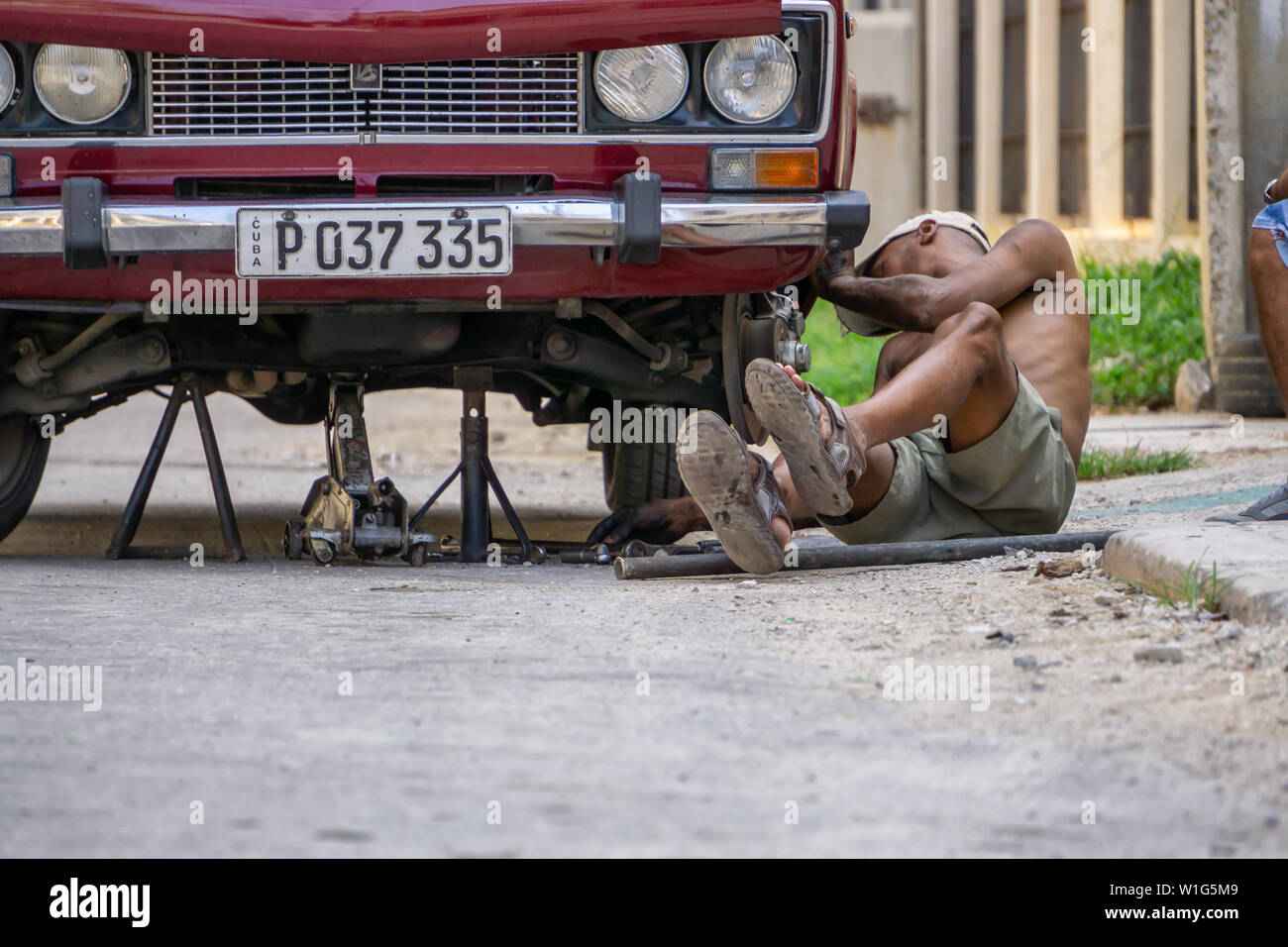 L'Avana, Cuba - Maggio 17, 2019: Sporco auto cubano meccanico è lavorare sotto il veicolo per le strade della vecchia Havana City durante una calda giornata di sole. Foto Stock