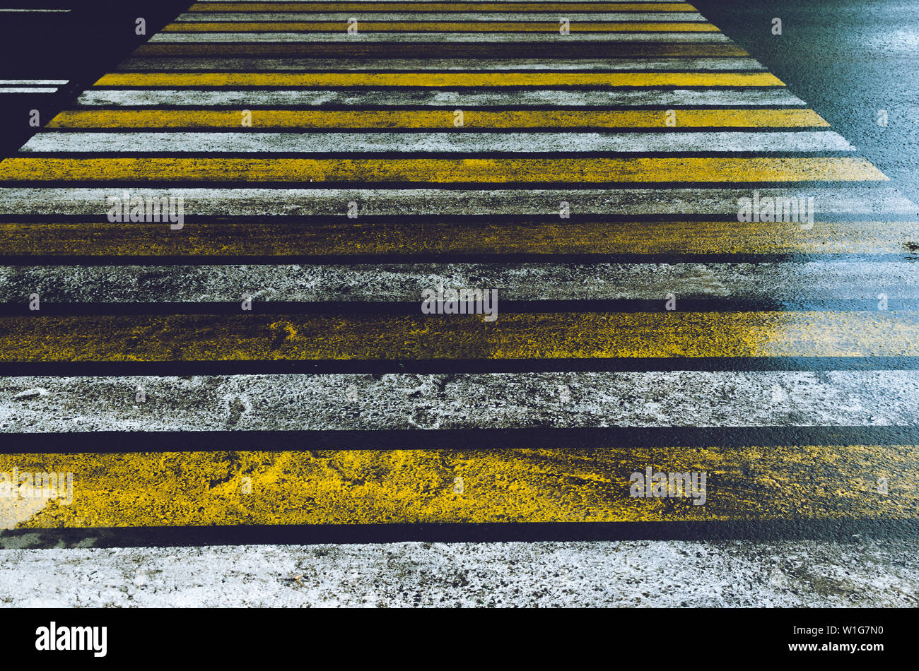 Strada sdrucciolevole con un attraversamento pedonale dipinte in giallo e bianco Zebra con abbagliamento dopo la pioggia. Foto Stock