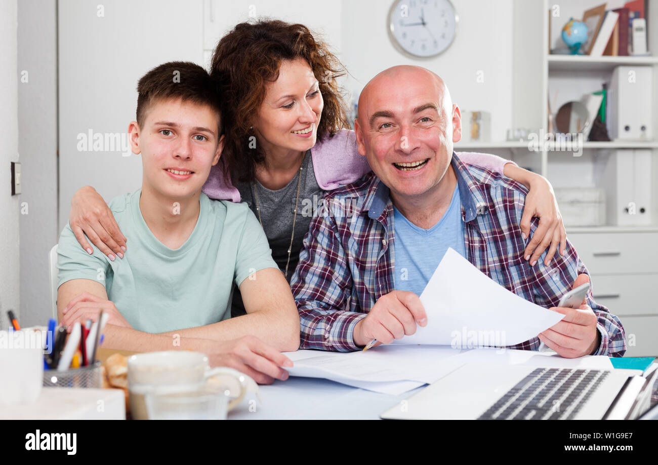 Ritratto di famiglia felice di tre con nostro figlio adolescente analizzando le loro finanze con documenti a casa Foto Stock