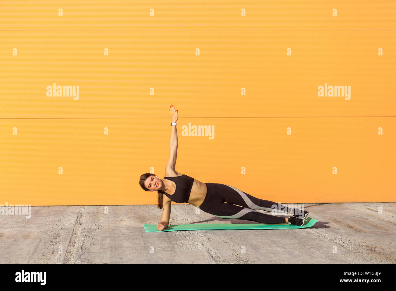 Giovane sportivo da donna attraente la pratica dello yoga, facendo esercizio vasisthasana, laterale plank pongono sui gomiti, lavoro, indossare abbigliamento sportivo nero, all'aperto, Foto Stock