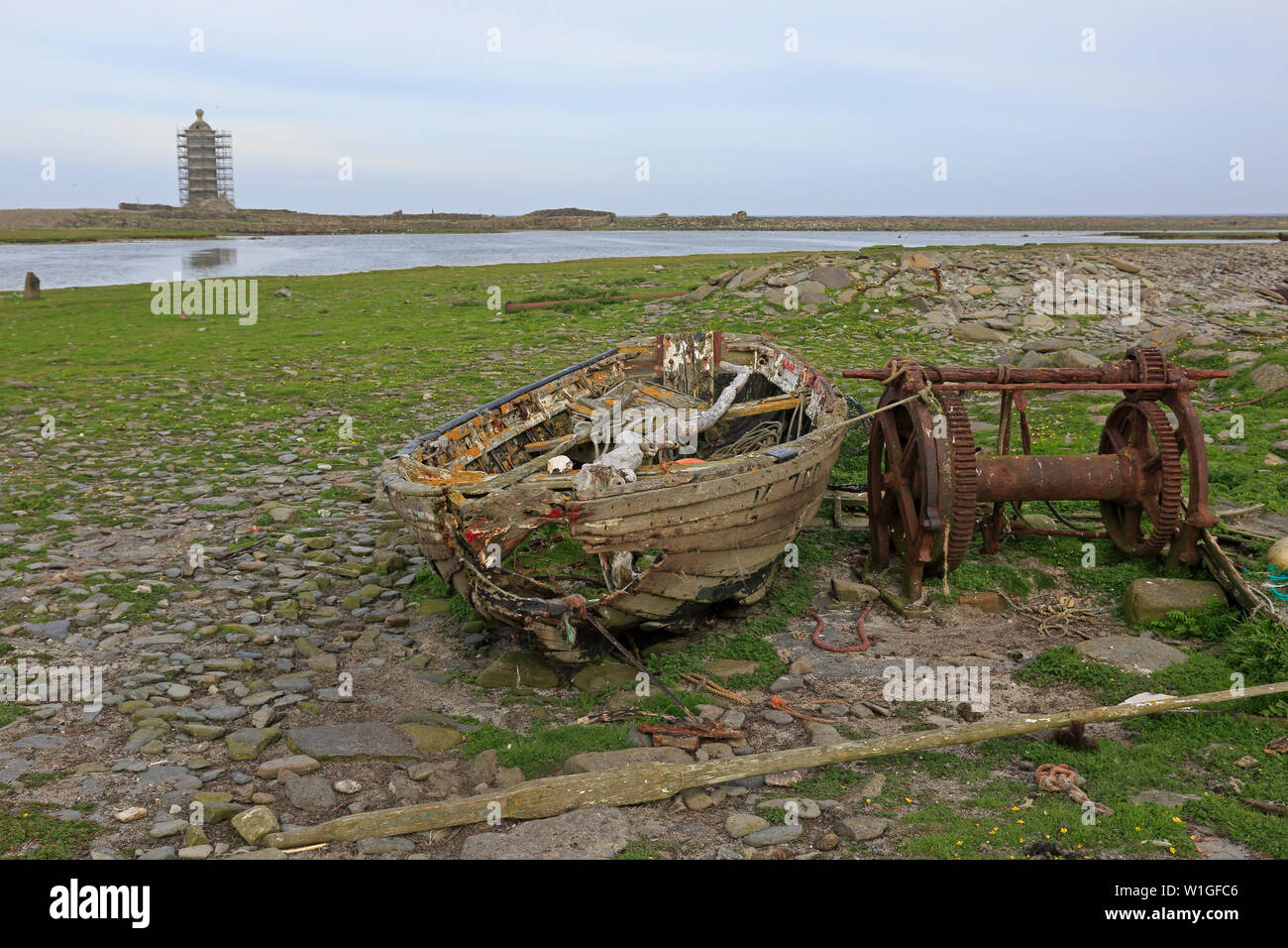Abbandonato vecchia barca da pesca e il verricello con il vecchio faro in background North Ronaldsay Isole Orcadi Scozia Scotland Foto Stock