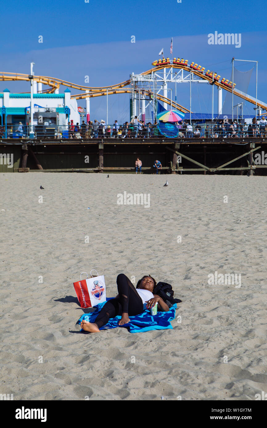 Lonely donna a prendere il sole nella spiaggia di Santa Monica. Dietro Pacific Park Parco divertimenti in Santa Monica Pier, Los Angeles, California Foto Stock