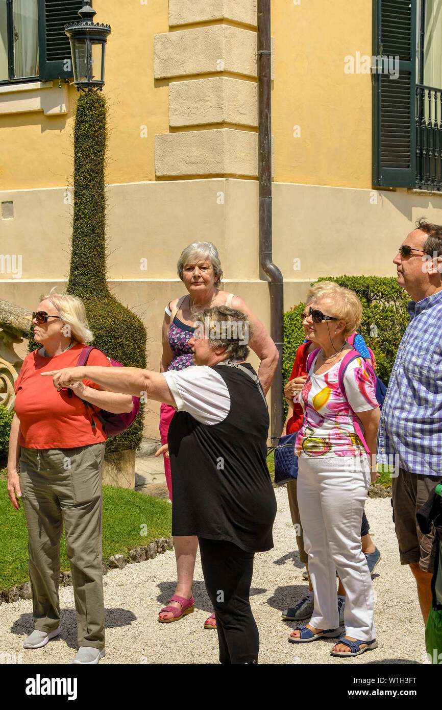 LENNO, LAGO DI COMO, Italia - Giugno 2019: Tour guida sottolineando qualcosa di interesse per un gruppo di visitatori nel parco della Villa del Balbianello a L Foto Stock