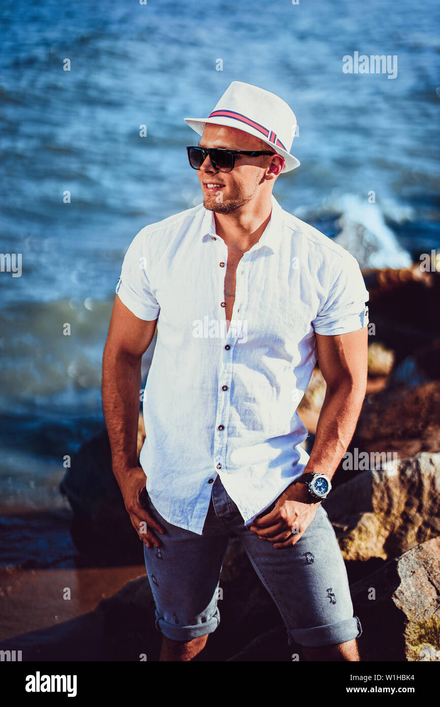 L'uomo presso il resort in una t-shirt, occhiali da sole e cappello sullo sfondo del mare che guarda lontano dalla telecamera. Foto Stock