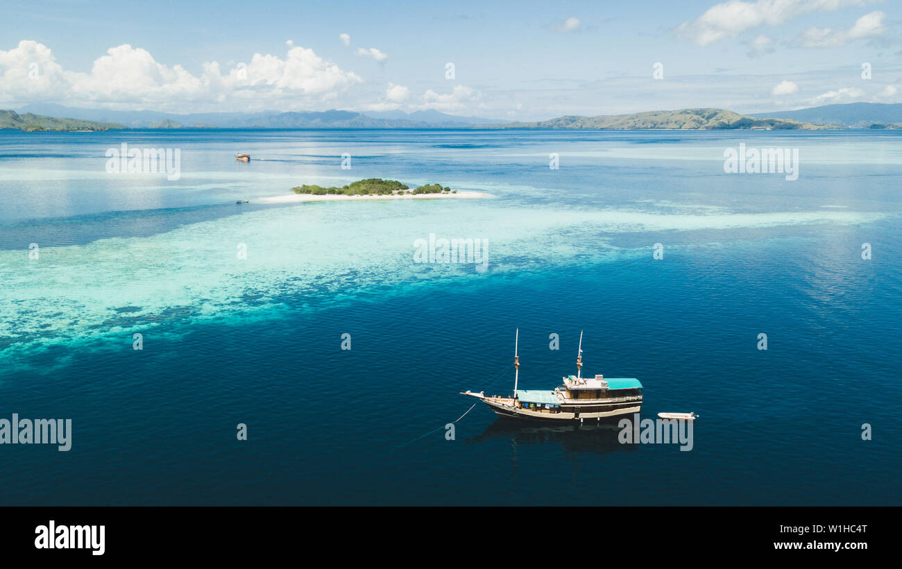 Crociera di Lusso in barca a vela vicino a Coral reef atoll isola con incredibile bianca spiaggia tropicale e le montagne sull orizzonte. Vista aerea. Nautica di lusso travel Foto Stock