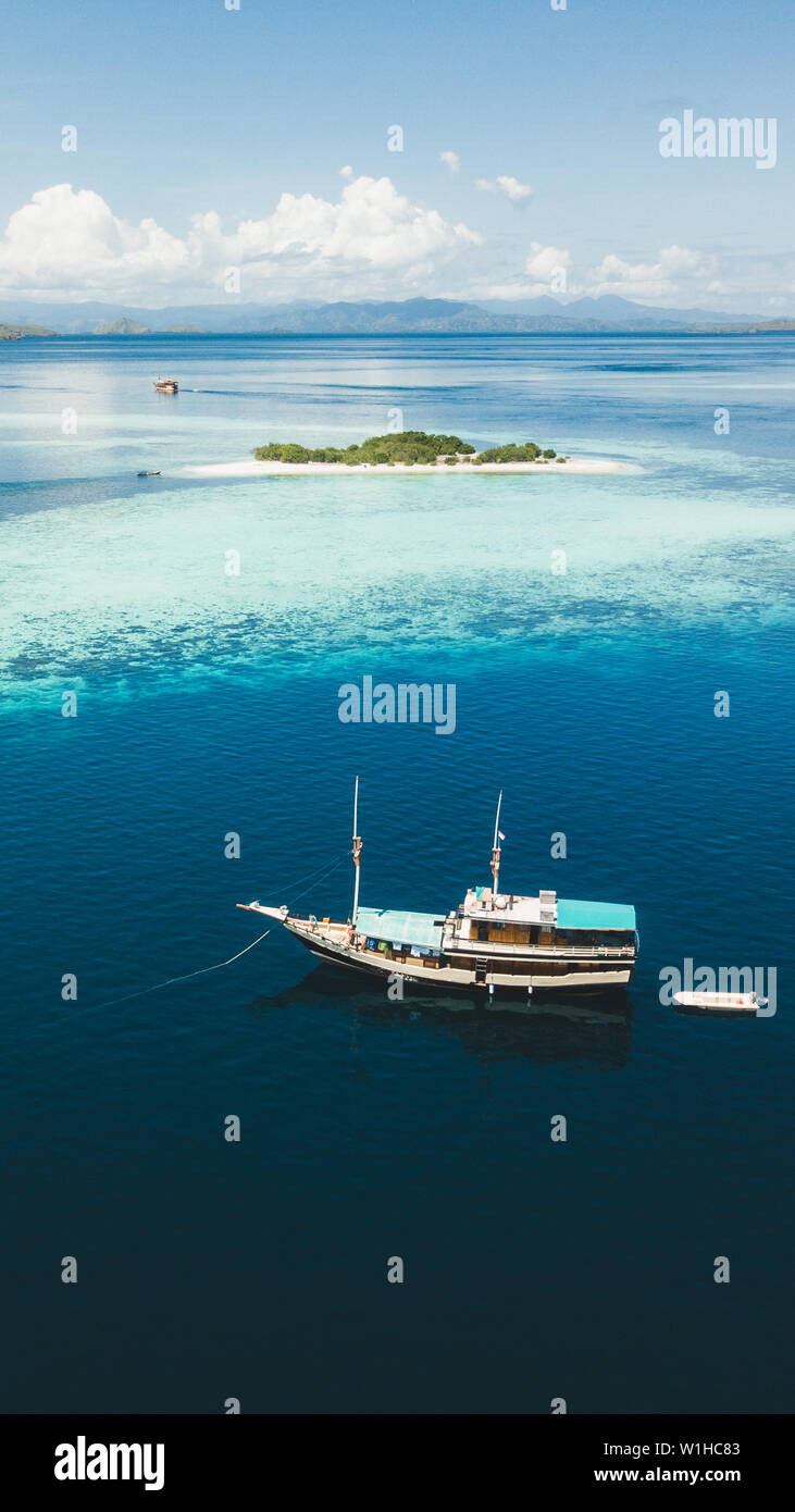Crociera di Lusso in barca a vela vicino a Coral reef atoll isola con incredibile bianca spiaggia tropicale e le montagne sull orizzonte. Vista aerea. 16:9 per lo schermo del telefono Foto Stock