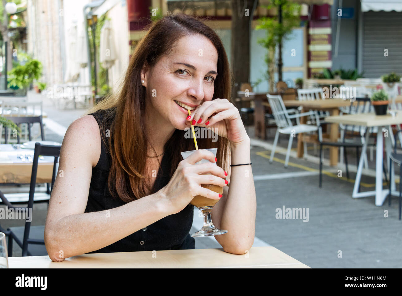 Ritratto di una donna matura, 40s, avente un freddo freddo cappuccino caffè seduti all'aperto in cerca della fotocamera. Foto Stock