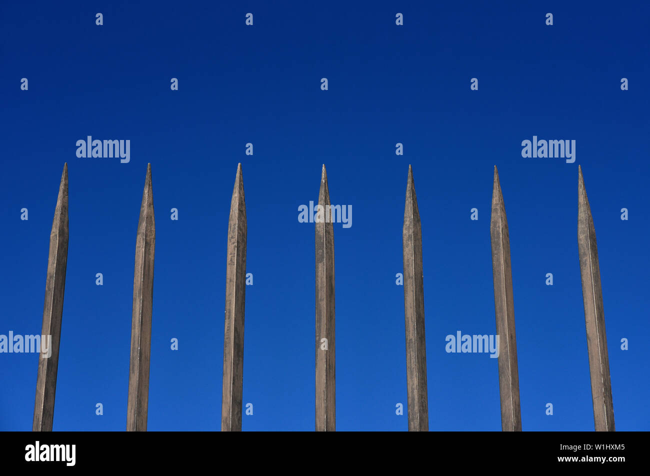 Recinzione in acciaio barriera con barre appuntite contro il cielo blu. Concetto di reclusione, ostacolo, sicurezza di protezione Foto Stock