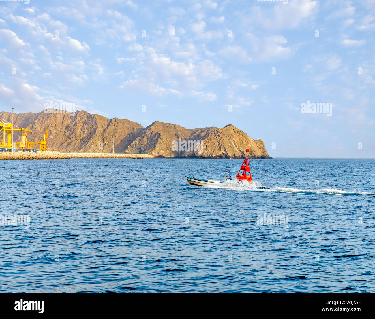 Velocità barca da pesca spostandosi a destra accanto a una boa di colore rosso nei pressi di Porta Muttrah, Muscat Oman. Foto Stock