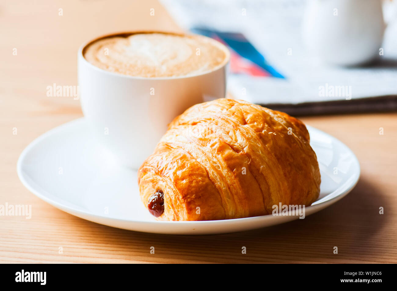 Una tazza di caffè e un croissant su una piastra bianca Foto Stock