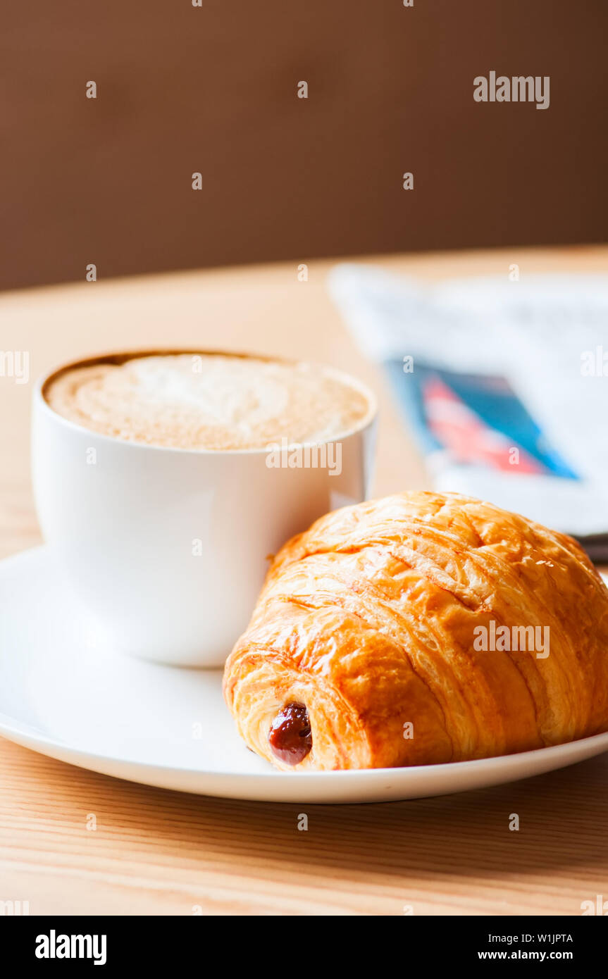 Una tazza di caffè e un croissant su una piastra bianca Foto Stock