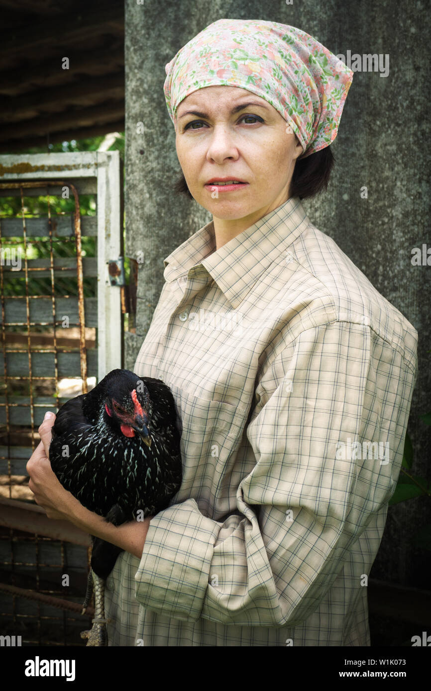 Contadina in abbigliamento uomo, tenendo in mano un pollo nero nelle sue mani nella rurale scena. Foto Stock
