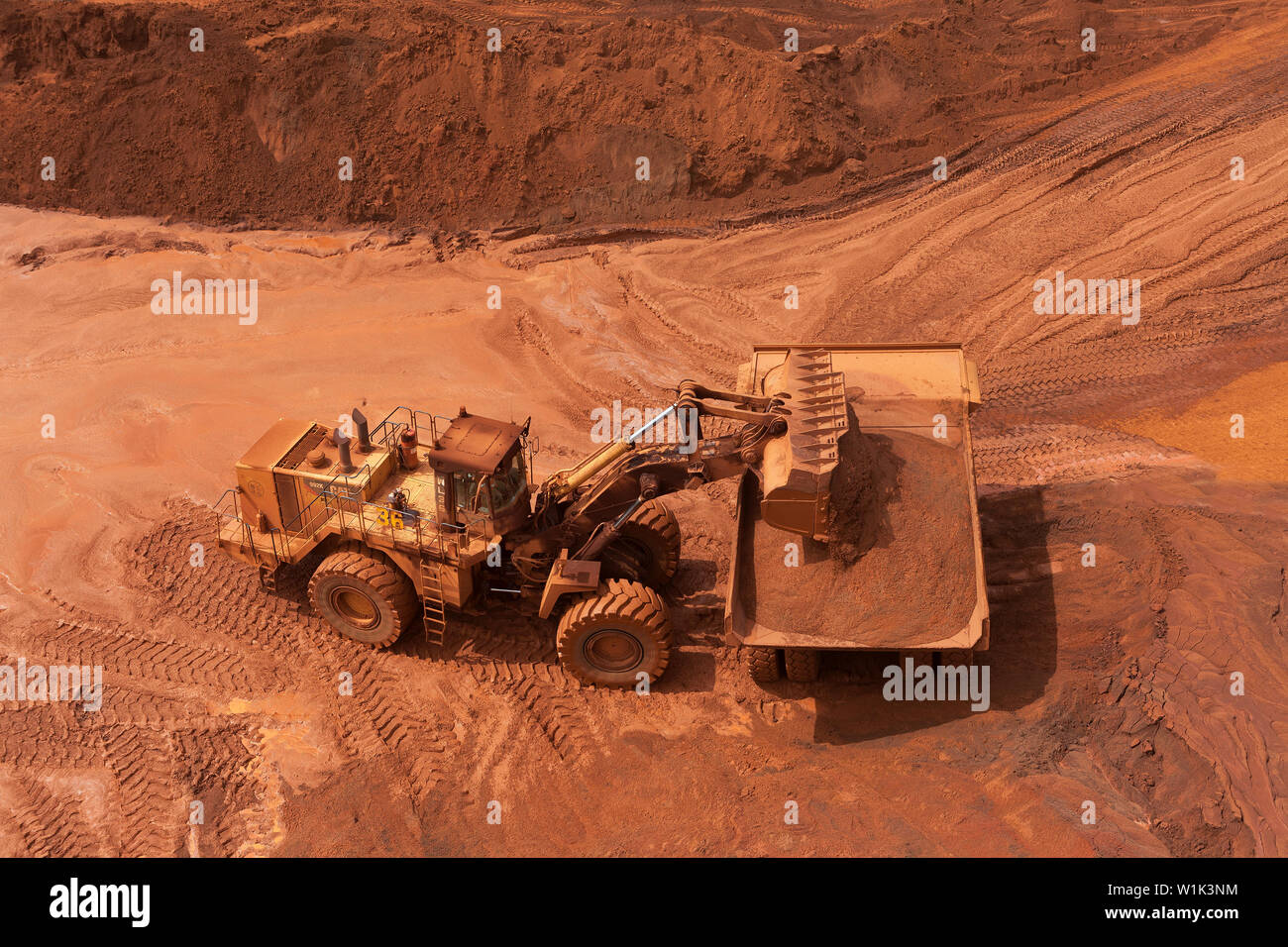 Le operazioni di data mining per il trasporto e la gestione di minerale di ferro. Sulle ammende raccoglitore per caricatore frontale di minerale di caricamento in autocarro con pianale di scarico prima del trasporto ferroviario al porto Foto Stock