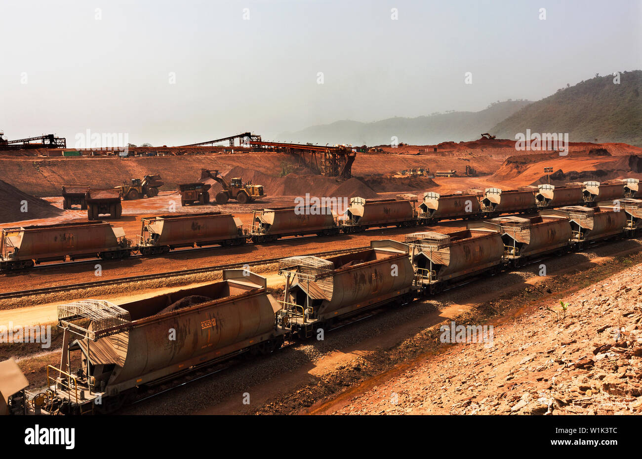 Treno ferroviario operazioni su miniera di minerale di ferro. Treno minerale caricato su circuito ferroviario in attesa di lasciare il porto. Stoccaggio delle scorte dietro il treno in fase di carico. Foto Stock