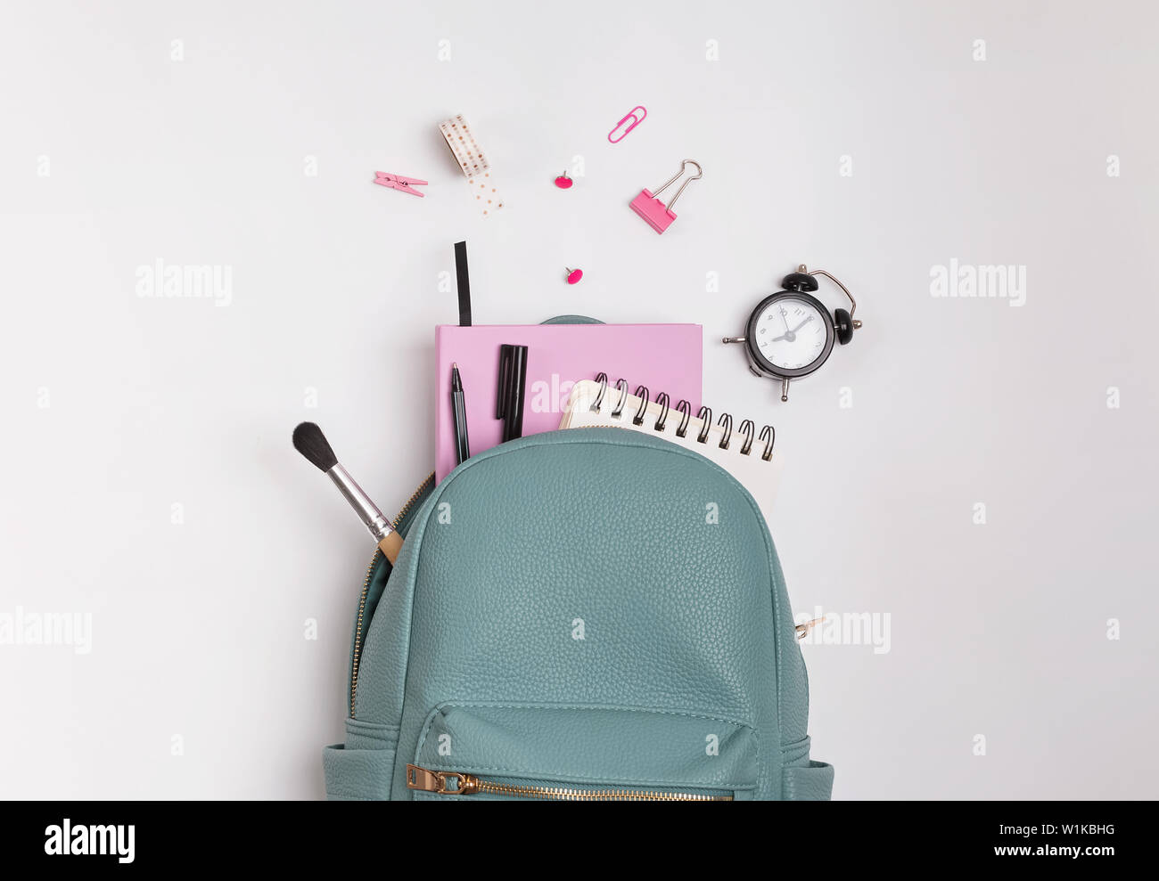Studente di zaino con differenti articoli di cancelleria e forniture di studio sullo sfondo bianco, vista dall'alto. Si torna a scuola concetto. Foto Stock