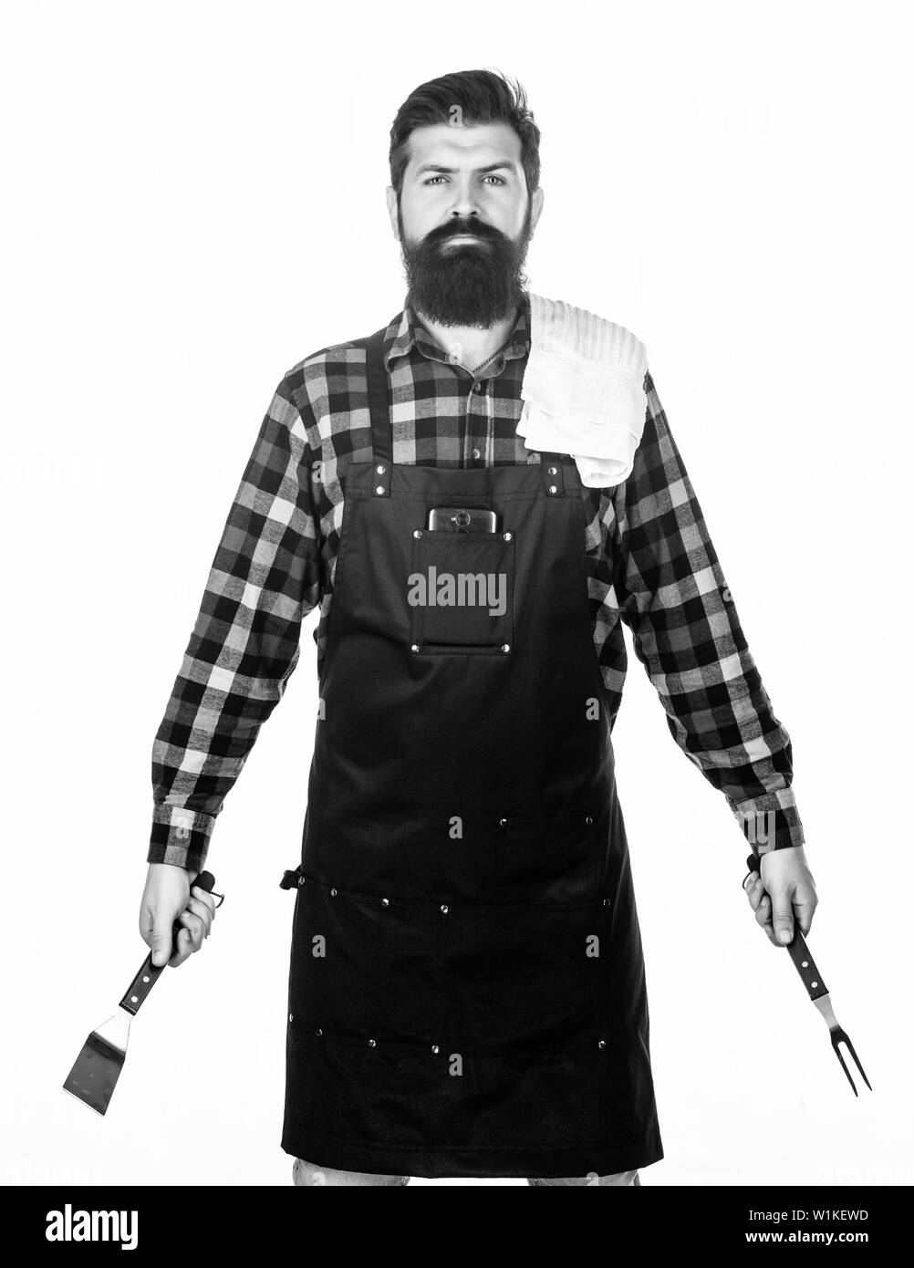 La tostatura e la cottura alla griglia di cibi. Man tenere utensili di cottura barbecue. Strumenti per la tostatura di carne all'esterno. Per picnic e barbecue. La cottura della carne nel parco. Barbecue master. Barbuto hipster indossare il grembiule per barbecue. Foto Stock