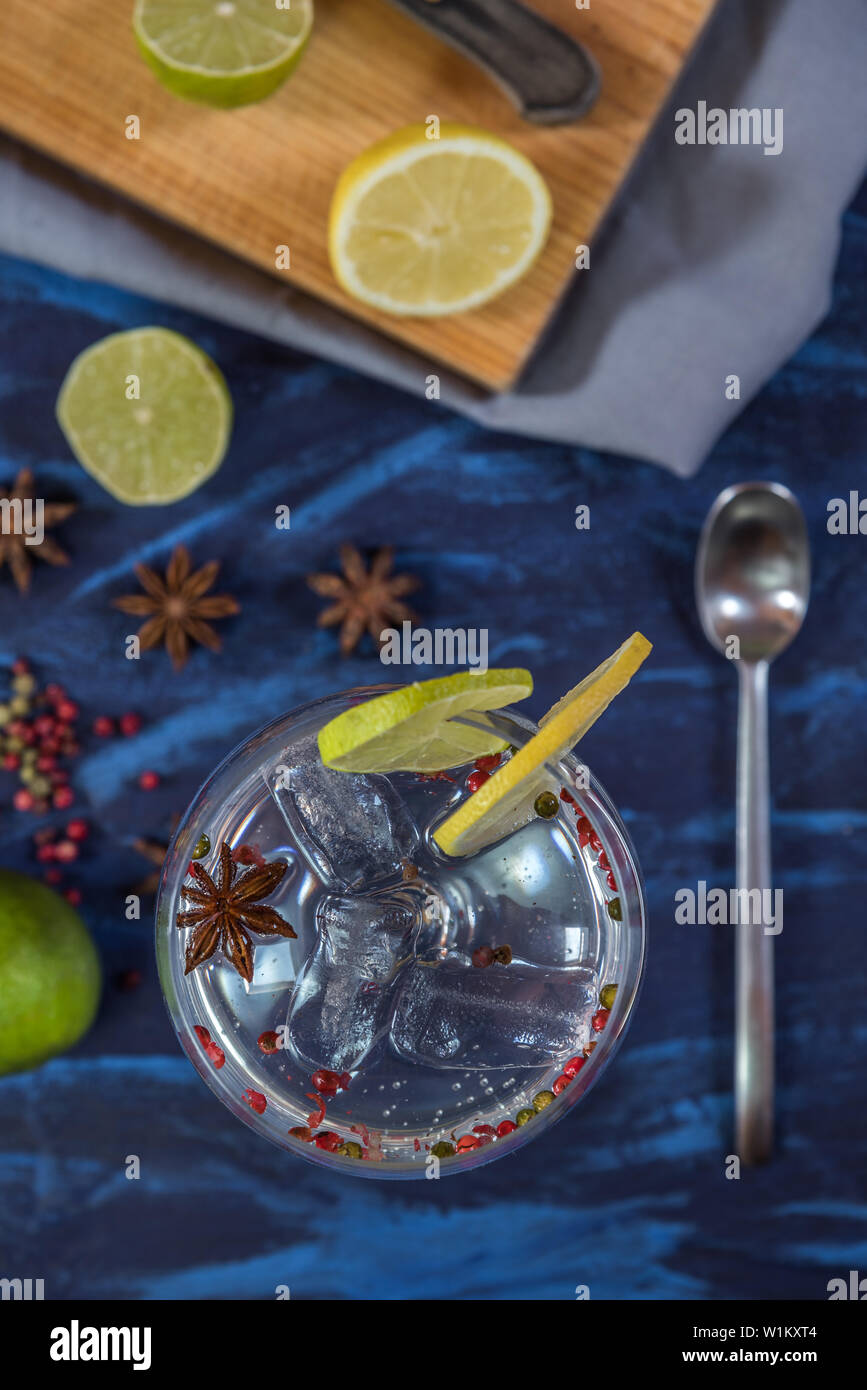 Il gin tonic in un bicchiere di vetro con fettine di lime e limone,pepe rosa e anice su un blu e nero sfondo rustico Foto Stock