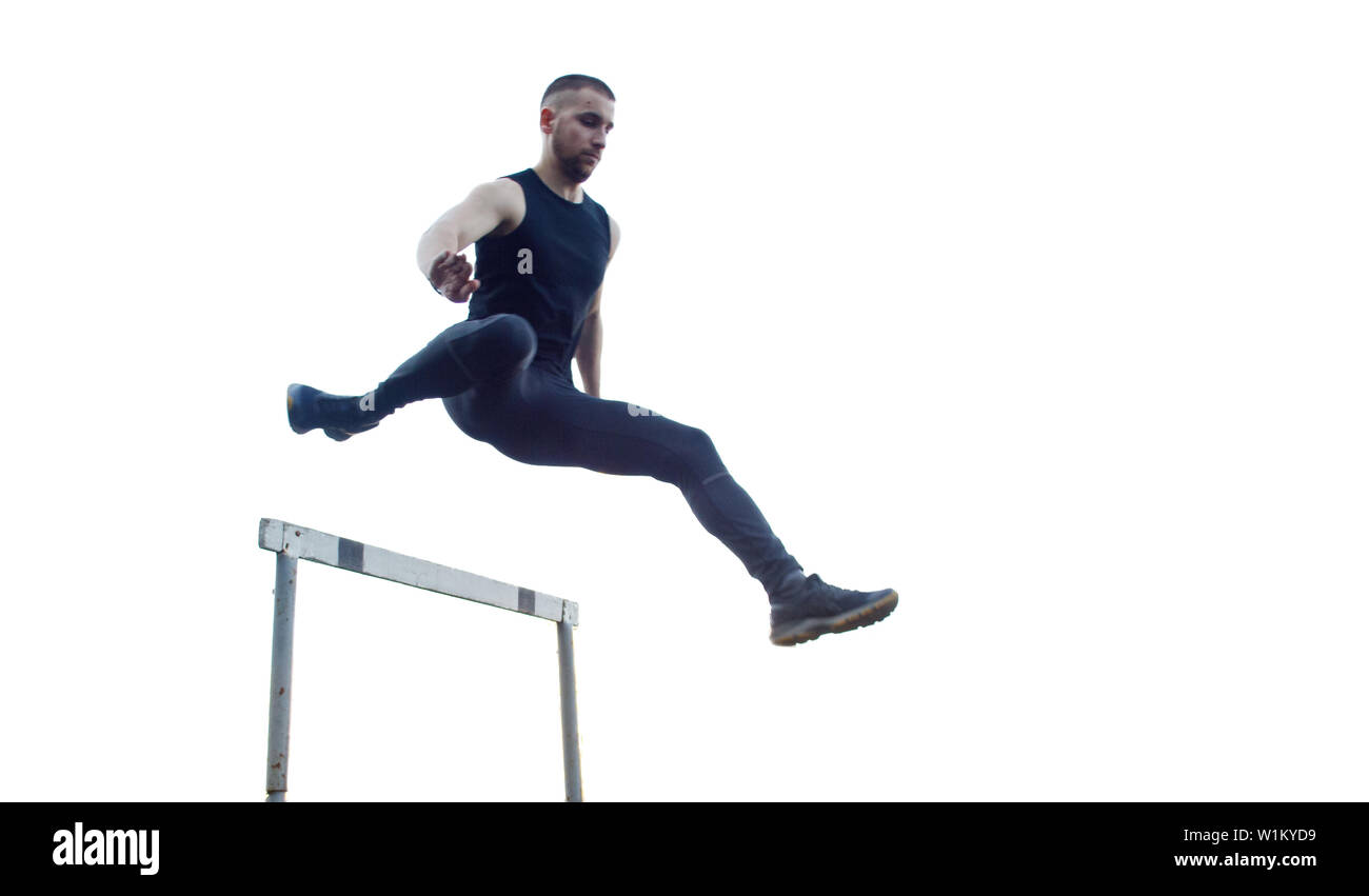 Un maschio caucasico in un salto oltre una barriera. in esecuzione sul Stadium. La via e il campo runner in sport uniforme in volo. energica attività fisica. Foto Stock