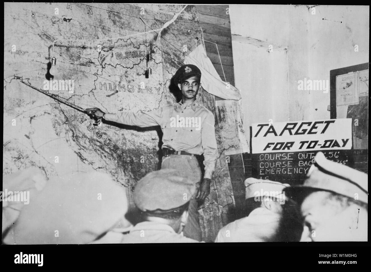 Con un funzionario dando loro puntatori da una mappa gigante, piloti di un American P Mustang caccia bombardiere gruppo imparano il loro 'target per oggi' durante un briefing in corrispondenza di una base in Italia. Sia la mappa e la briefing grafico (a destra) indicano un altro obiettivo in Germania sarà presto sul lato ricevente di loro pallottole e bombe. Gli uomini sono membri del XV U.S. Army Air Force, i cui piani volare come parte del Mediterraneo Allied Air Force, ca. 09/1944 Foto Stock